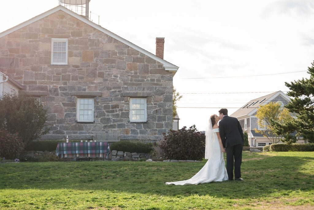 bride and groom in wedding attire walk past the stonington lighthouse museum on their wedding day