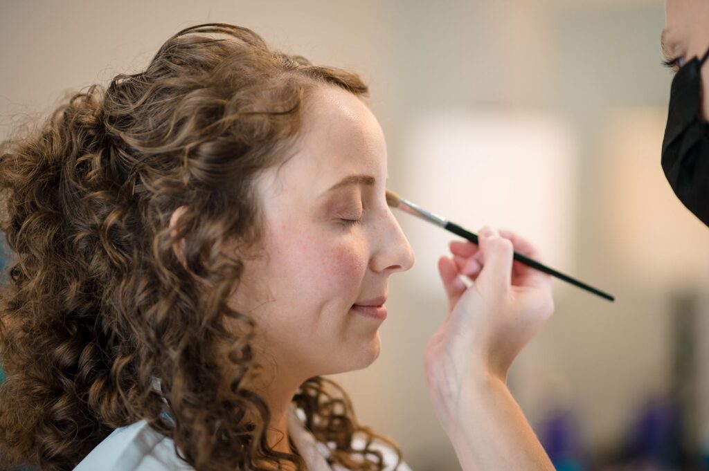 makeup artist applies eye shadow to bride's face using a long thin brush