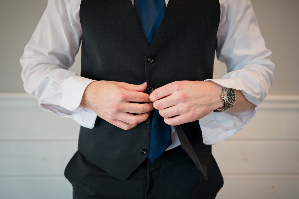 groom wearing a suit buttons a navy blue vest