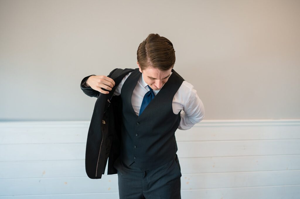 groom wearing a navy suit puts his jacket on