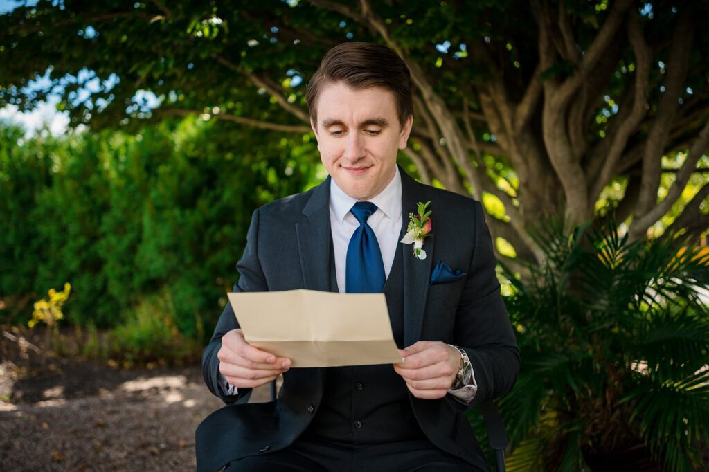 Groom sits under a tree at the hounds in stonington reading a letter from his bride