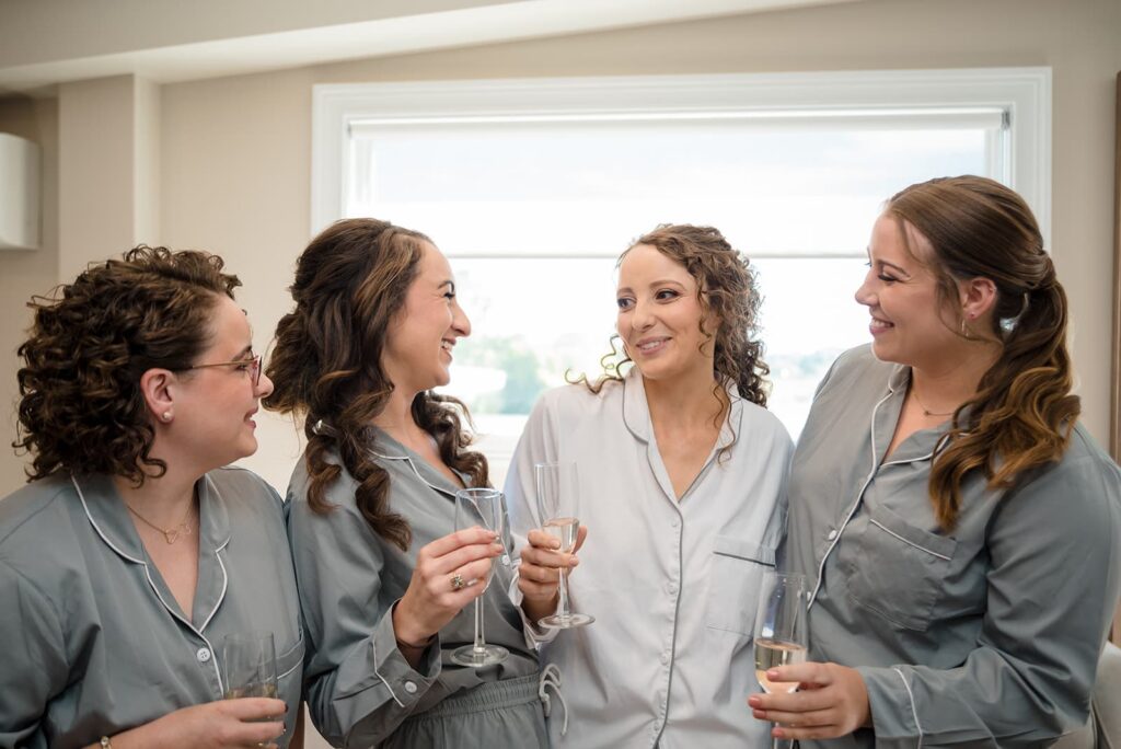 bride and three bridesmaids smile at one another while toasting